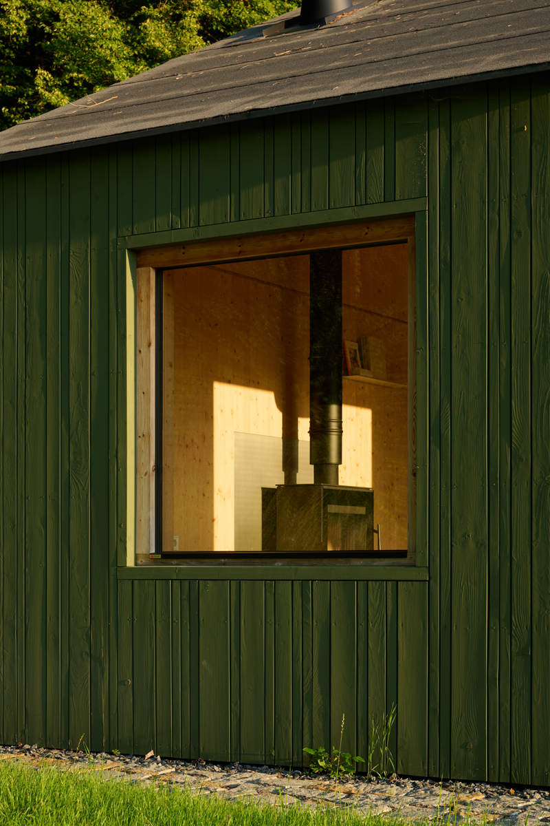 Detail tmavozelené fasády chaty Bebech s malým čtvercovým oknem ukazuje jednoduchost a dokonalé řemeslo.