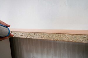 Muž opravující hranu nábytkové desky pomocí lepidla.