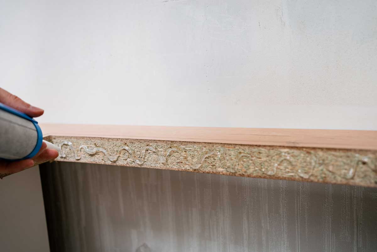 Muž opravující hranu nábytkové desky pomocí lepidla.