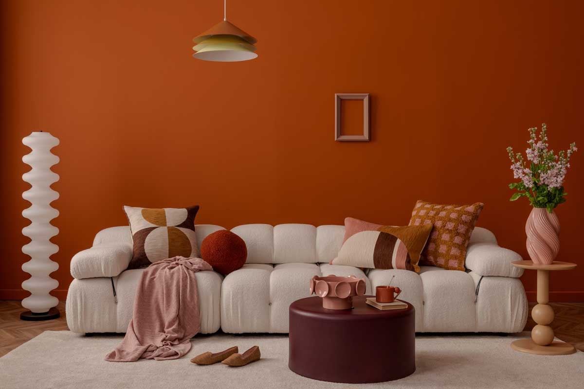 Obývací pokoj s oranžovou terakotovou stěnou, světle krémovou pohovkou a dekoracemi v teplých barvách.