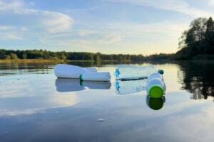 Plastové lahve plovoucí na hladině jezera s lesem v pozadí při západu slunce.
