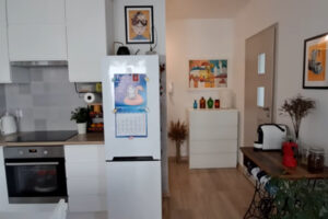 Výhled z kuchyně do předsíně s bílou komodou, barevnými vázami a moderními doplňky.