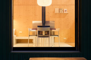 Večerní pohled do prosvětleného interiéru chaty s dřevěným obkladem a jídelním stolem.