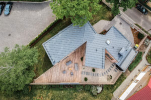 Letecký pohled na dům s plechovou střechou, dřevěnou terasou a okolní zahradou.