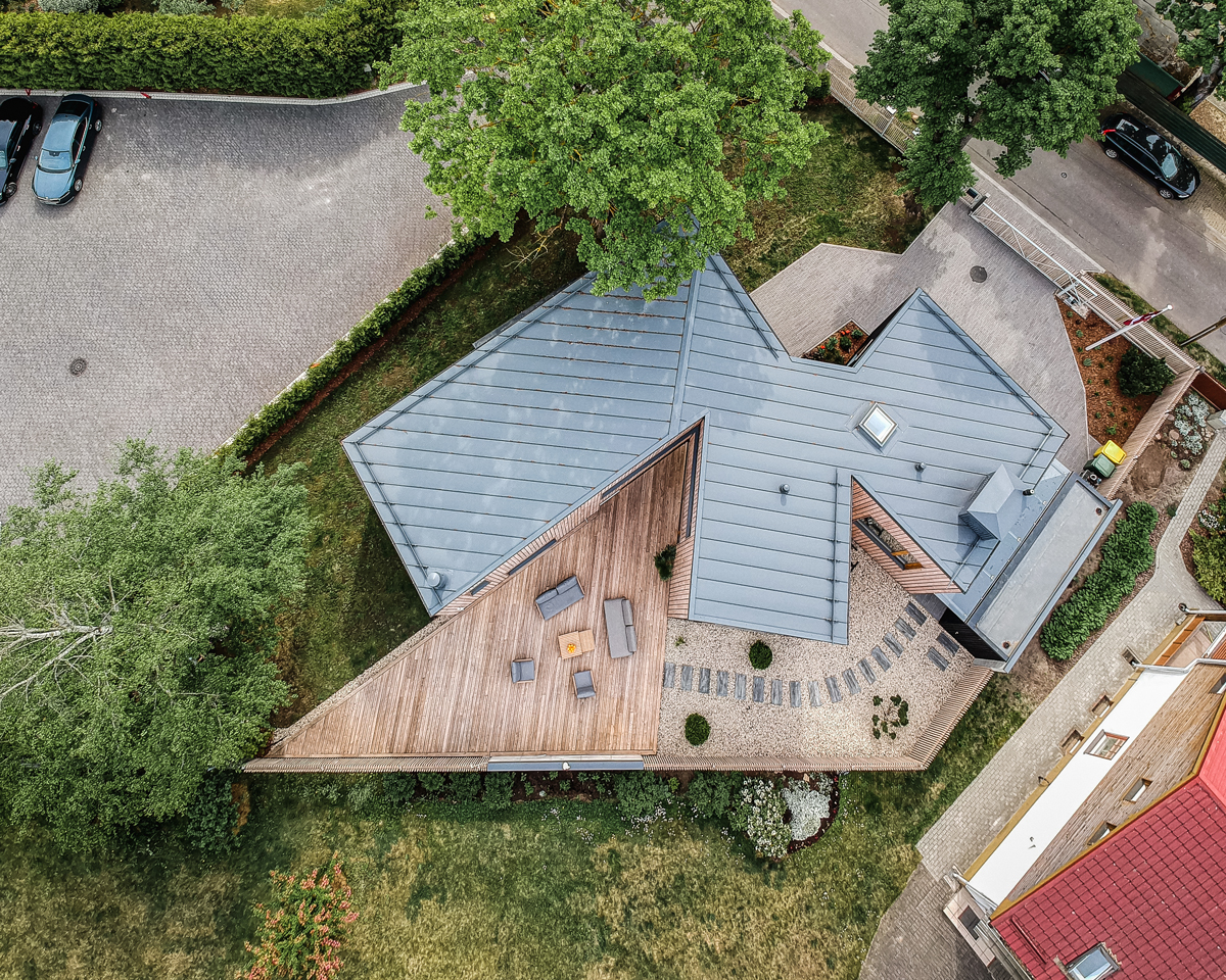Letecký pohled na dům s plechovou střechou, dřevěnou terasou a okolní zahradou.