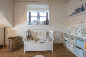 Světlý dětský pokoj s dřevěnou lavicí, košem a policí plnou hraček v jemných pastelových barvách.