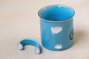 Modrý hrnek s odlomeným uchem připravený k vyřazení.
