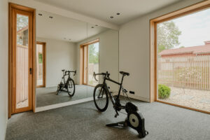 Domácí posilovna s cyklistickým trenažérem a velkými prosklenými dveřmi do zahrady.
