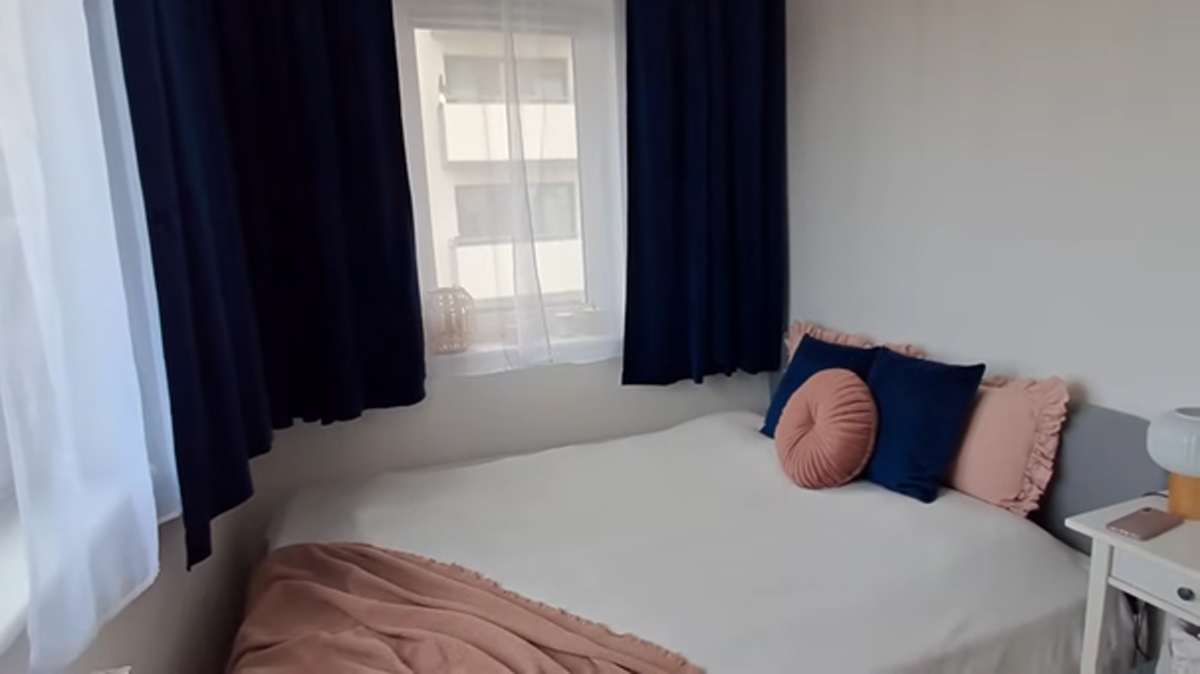 Ložnice s bílou postelí, tmavě modrými závěsy a pastelovými doplňky.