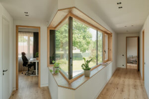 Interiér domu s pracovnou a rohovým oknem v chodbičce, lemovaným dřevěným ostěním.