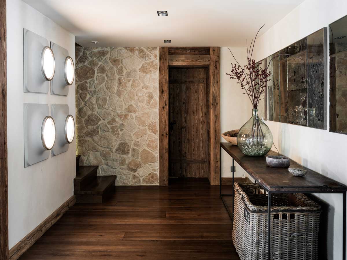 Chodba v Chalet 1936 s přírodní kamennou stěnou, recyklovaným dřevem a vintage dekoracemi v duchu recyklace.