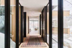 Prosklená chodba v moderní horské chatě s výhledem na zasněžený les.