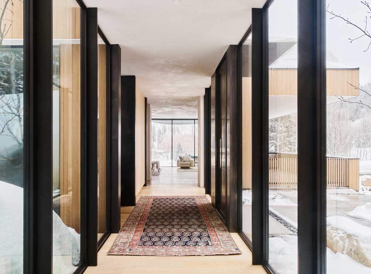 Prosklená chodba v moderní horské chatě s výhledem na zasněžený les.