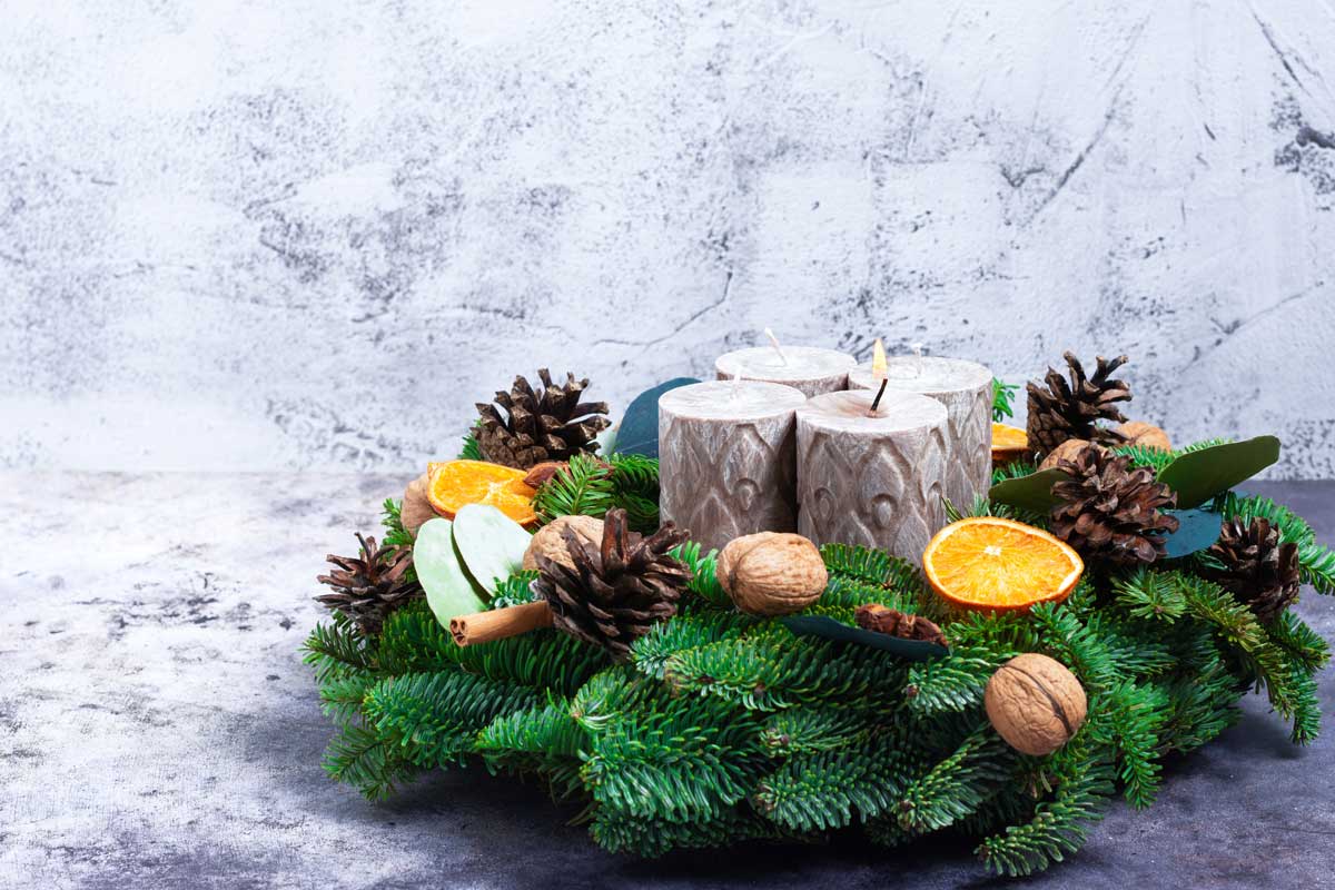 Přírodní adventní věnec z jehličí zdobený šiškami, sušeným ovocem, ořechy a dekoracemi z kůry působí autenticky a lesně.