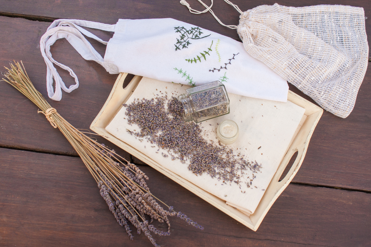 Domácí látkový pytlík s vyšitým dekorem a levandulí rozptýlenou na dřevěném podnose.