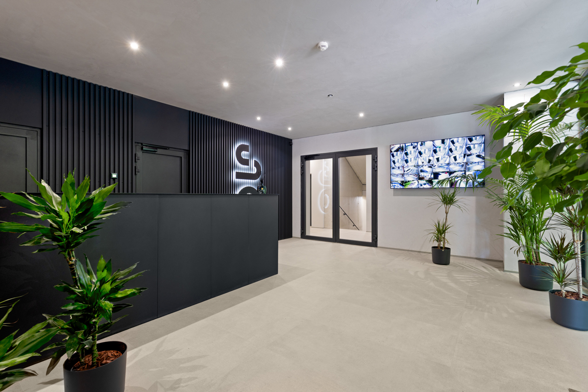 Designová recepce bytového domu SO.HOUSE s tmavým obkladem a živými rostlinami.