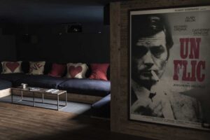Tmavá filmová místnost v Chalet 1936 s vintage plakátem a sedací soupravou z recyklovaných materiálů.