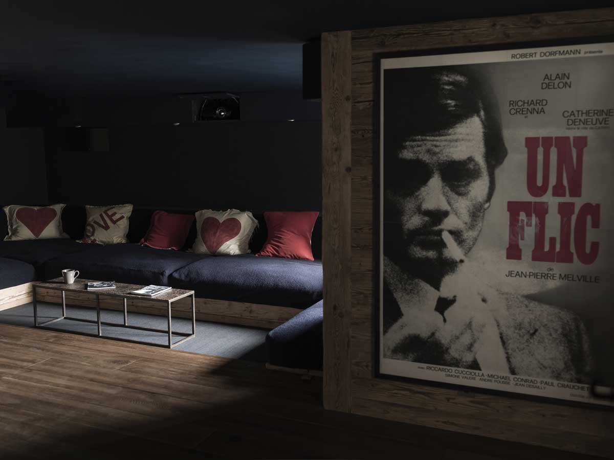 Tmavá filmová místnost v Chalet 1936 s vintage plakátem a sedací soupravou z recyklovaných materiálů.