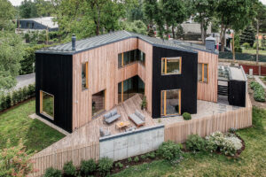 Letecký pohled na rodinný dům s dřevěnou fasádou a terasou ve tvaru klínu.