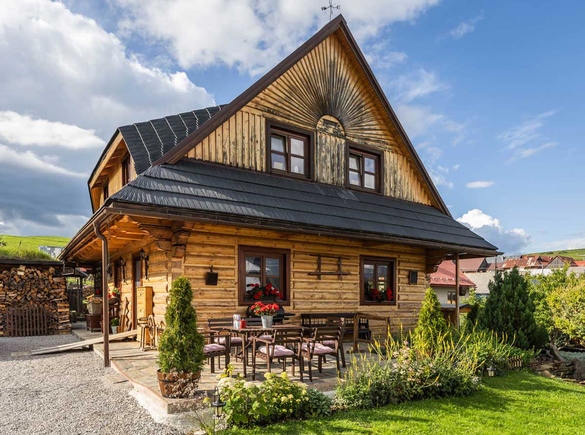 Exteriér dřevěné roubenky s bohatou zahradou, terasou a tradičními prvky, které odrážejí poctivou práci majitelů.