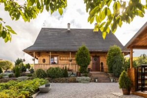 Hlavní vstup do roubeného domu obklopený zelení, dřevěnými prvky a pečlivě upravenou zahradou.