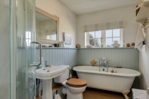 Světlá koupelna s volně stojící vanou, dřevěným obkladem a jemnými dekoracemi působí klidně a navozuje relaxační atmosféru rustikálního stylu.