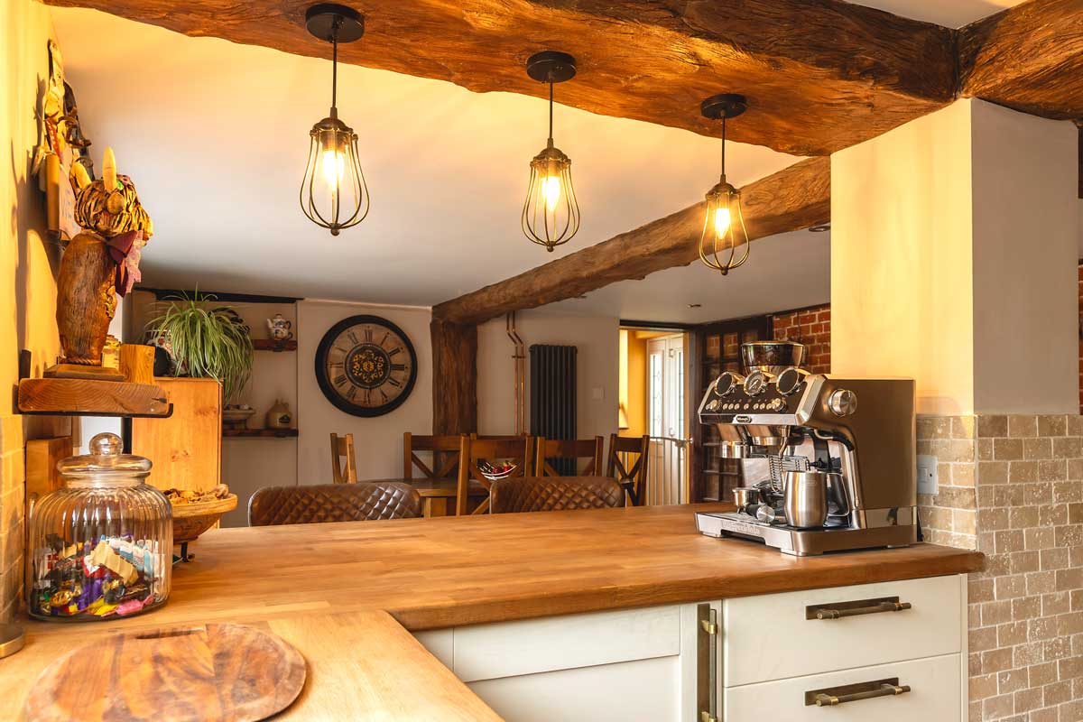 Bílá kuchyňská linka s dřevěnou deskou, závěsnými hrnky a praktickými doplňky ukazuje propojení funkce a teplého domácího designu.