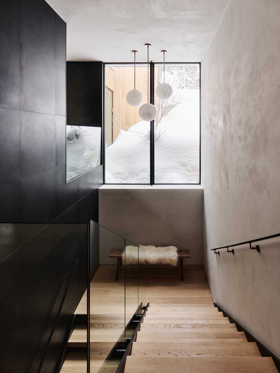 Minimalistické schodiště osvětlené velkým oknem a kulovými závěsnými svítidly.