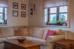 Útulný obývací pokoj s bílou rohovou sedačkou, dřevěnou truhlou po prarodičích a proutěnými doplňky.