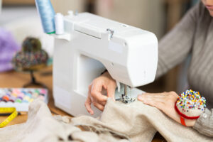 Šití látkového pytlíku na šicím stroji, detail na ruce a jehlu.