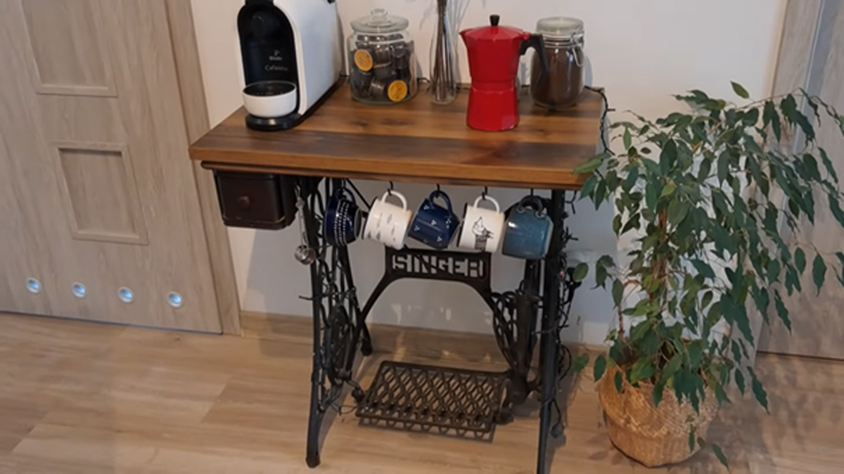 Retro stolek z podnoží šicího stroje s kávovarem, hrníčky a sklenicemi.
