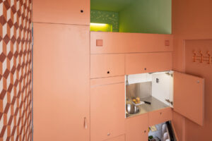 Detail vestavěné kuchyně v mikrobytě s integrovanými spotřebiči a nerezovým dřezem.