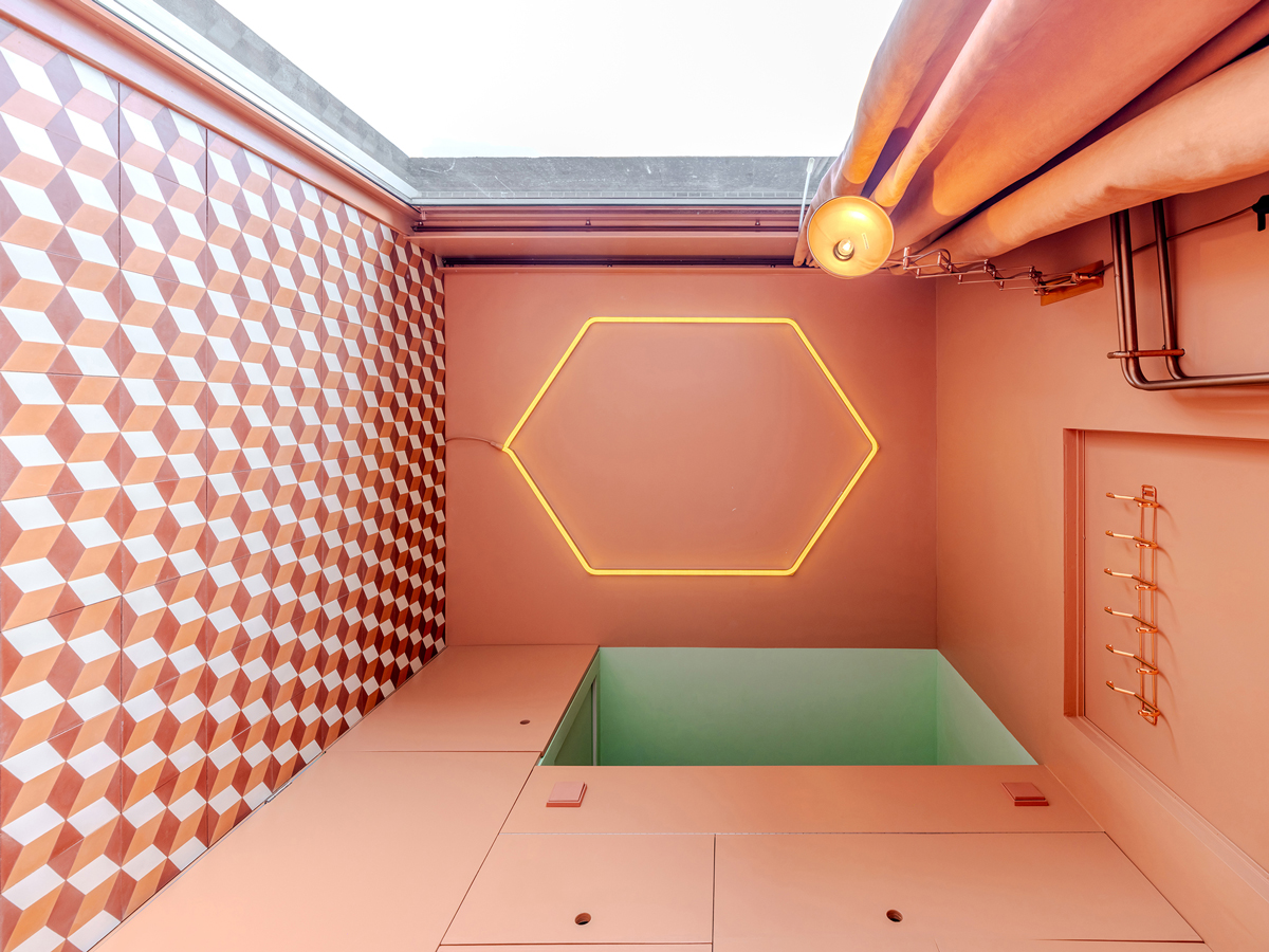 Detail stropu s hexagonálním světlem a oranžovo-bílým 3D obkladem.