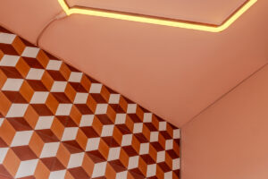 Detail stropu s neonovým světlem a barevně laděnou stěnou s geometrickým obkladem.