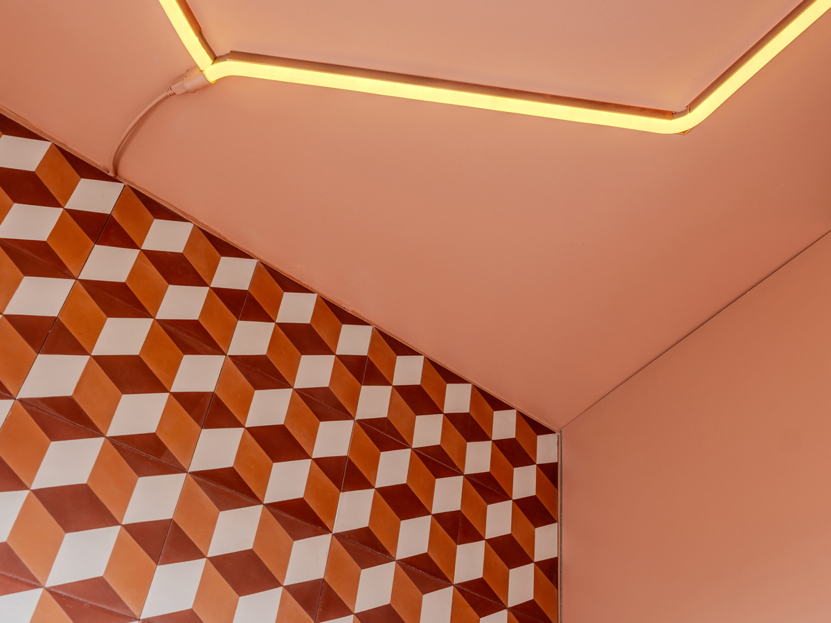 Detail stropu s neonovým světlem a barevně laděnou stěnou s geometrickým obkladem.