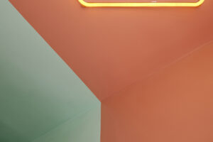 Detail stropu s barevným přechodem mezi oranžovou a zelenou plochou a svítícím neonem.