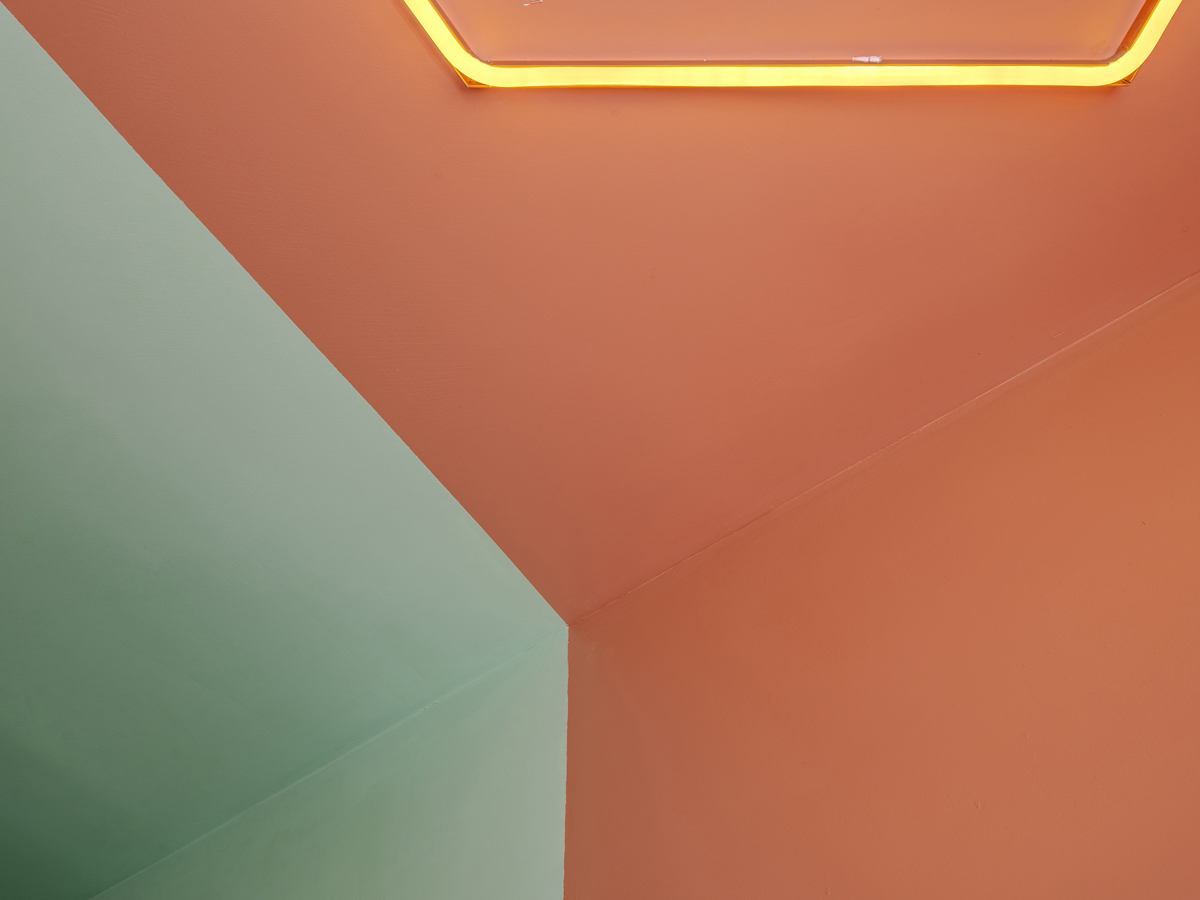 Detail stropu s barevným přechodem mezi oranžovou a zelenou plochou a svítícím neonem.
