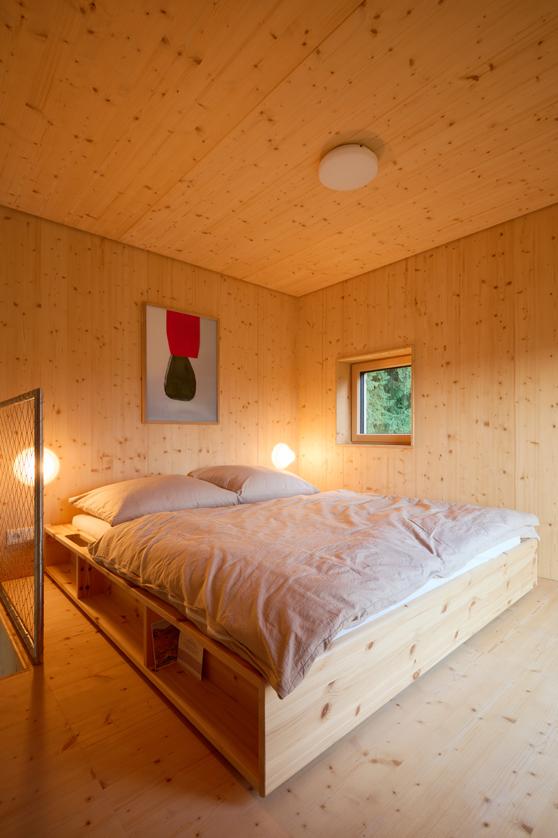 Ložnice z masivního dřeva působí hřejivě a klidně, večerní osvětlení dodává prostoru měkkou, téměř medovou atmosféru.