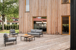 Dřevěná terasa se zahradním posezením u domu obloženého světlým dřevem.