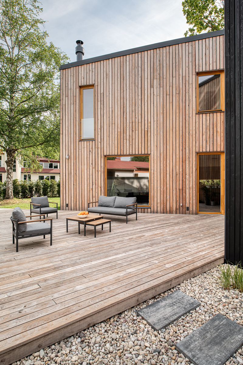 Dřevěná terasa se zahradním posezením u domu obloženého světlým dřevem.