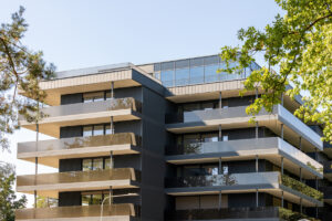 Moderní fasáda bytového domu s velkorysými terasami a skleněným zábradlím.