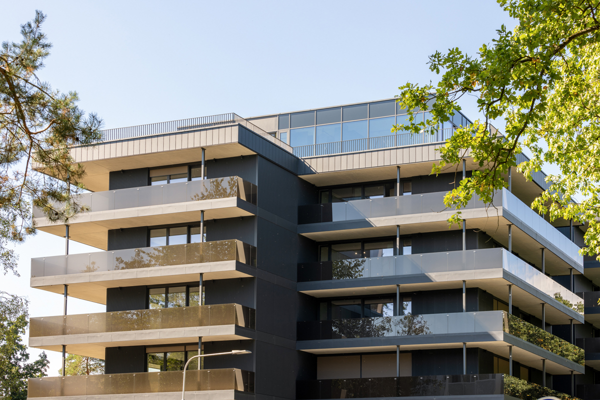 Moderní fasáda bytového domu s velkorysými terasami a skleněným zábradlím.