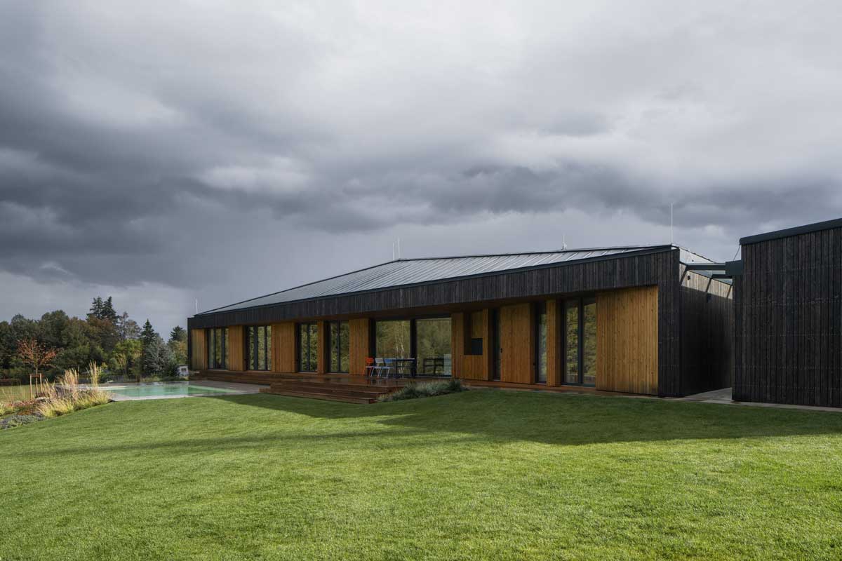 Travnatá zahrada s nízkým rodinným domem zasazeným do svažitého terénu