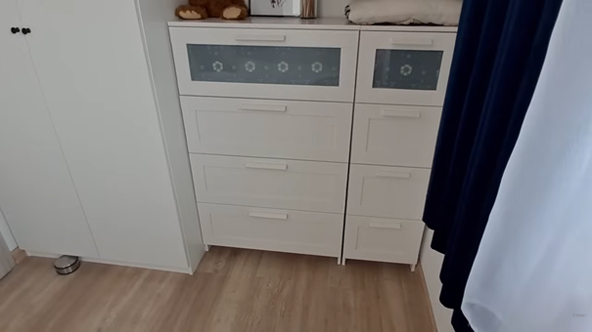 Komoda a skříň v malé ložnici s bílým nábytkem a dřevěnou podlahou.