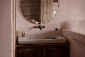 Recyklované kamenné umyvadlo a kulaté vintage zrcadlo v koupelně Chalet 1936 s přírodními povrchy.