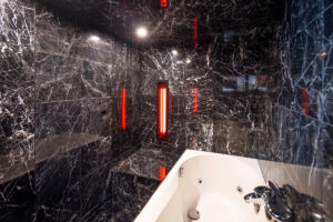 Interiér mini SPA se saunou a vířivkou obložený černým mramorem s červeným osvětlením.