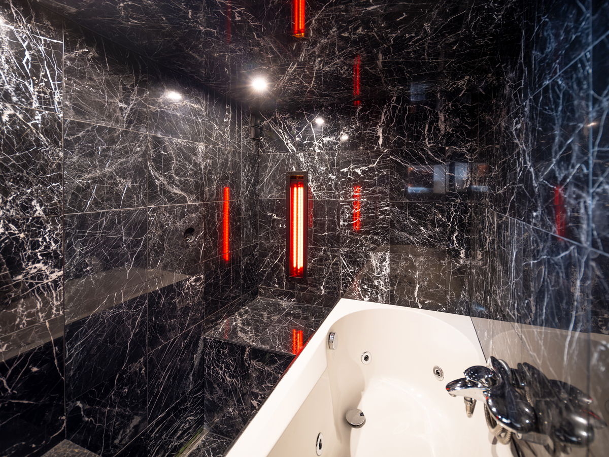 Interiér mini SPA se saunou a vířivkou obložený černým mramorem s červeným osvětlením.