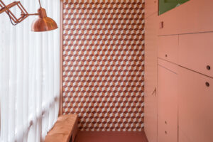 Interiér mikrobytu s oranžovými stěnami, velkým oknem a geometrickým obkladem.