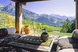 Výhled z terasy s rustikálním nábytkem na zelené svahy a jezero uprostřed hor.