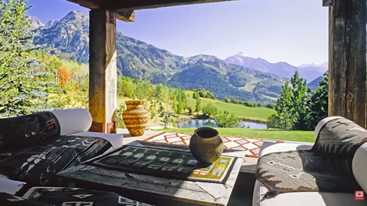 Výhled z terasy s rustikálním nábytkem na zelené svahy a jezero uprostřed hor.